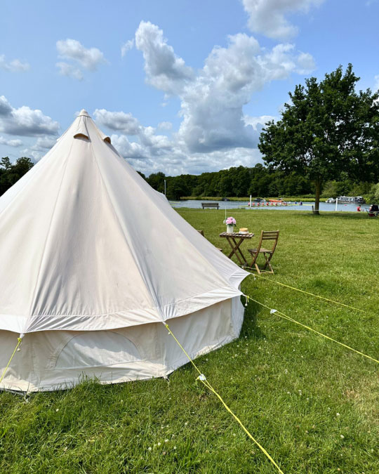 glamping tipee sits on a green field looking across to a river with rowers on it