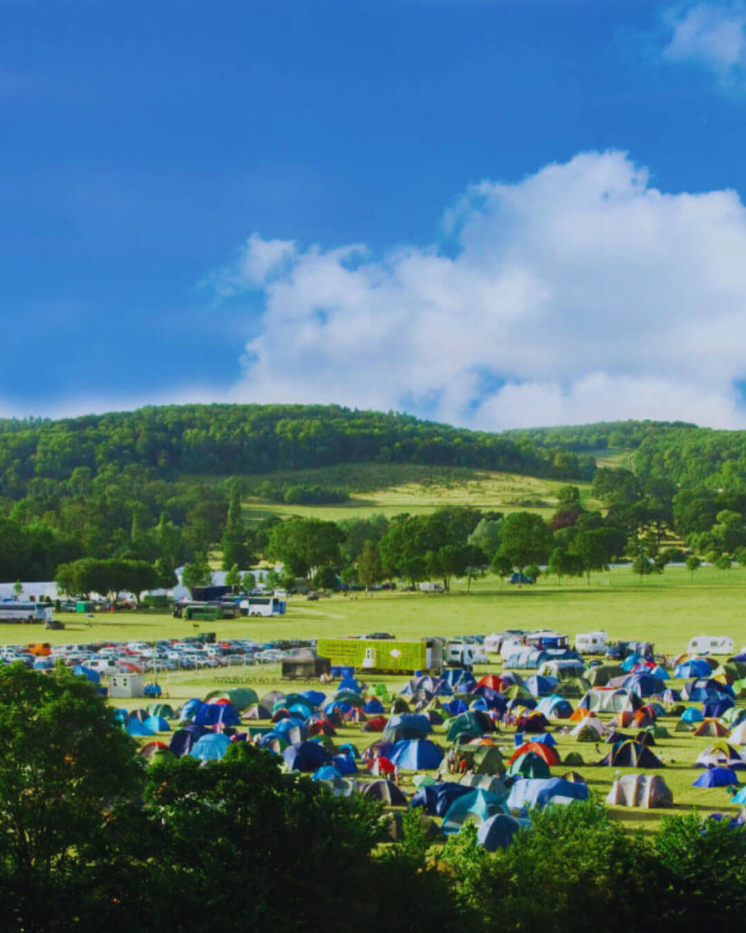 overview od campisute with multiple tents, green grass and tress and blue sky