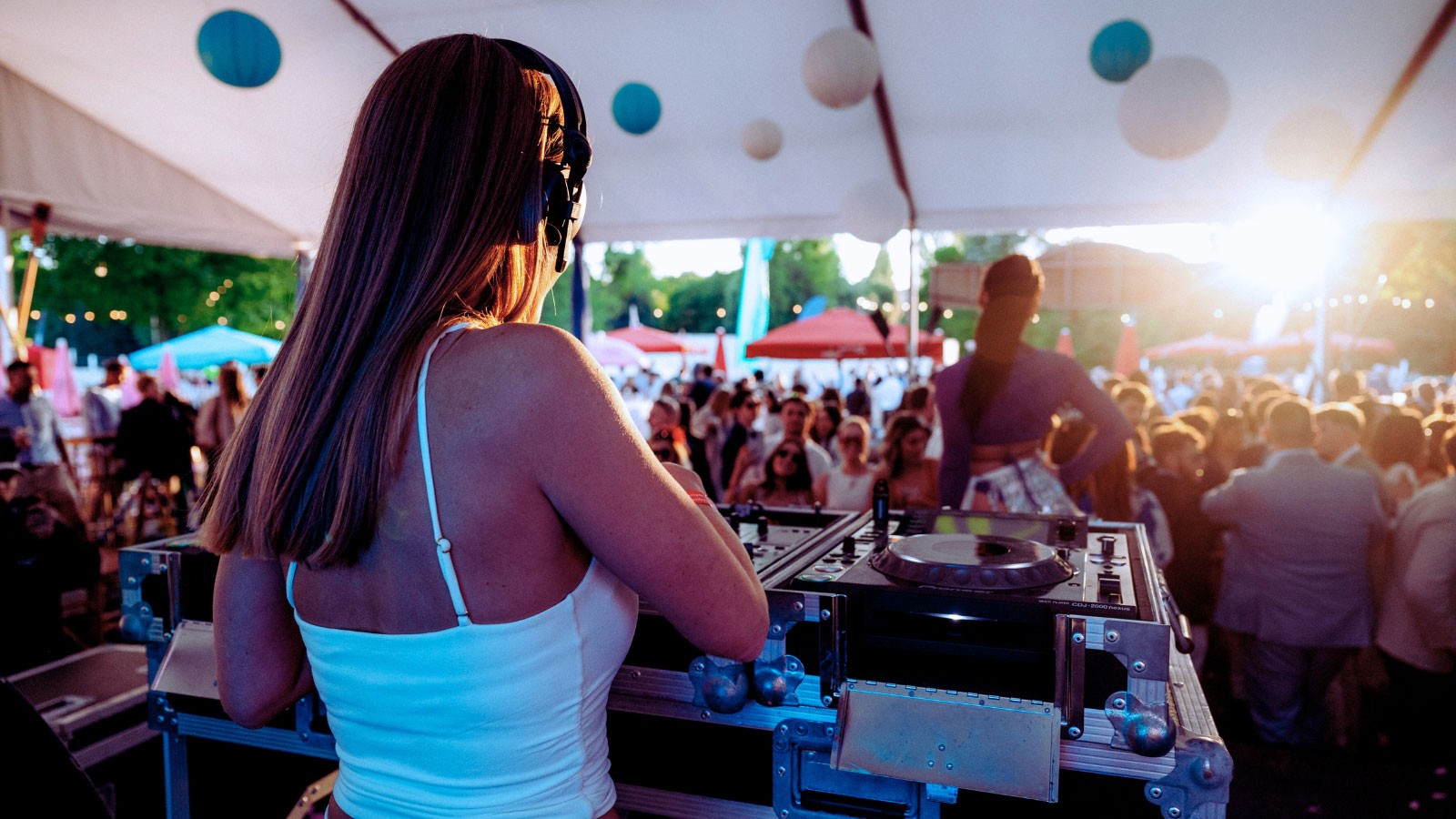 Female DJ playing to a crowd of people in a marquee with the sun setting in background