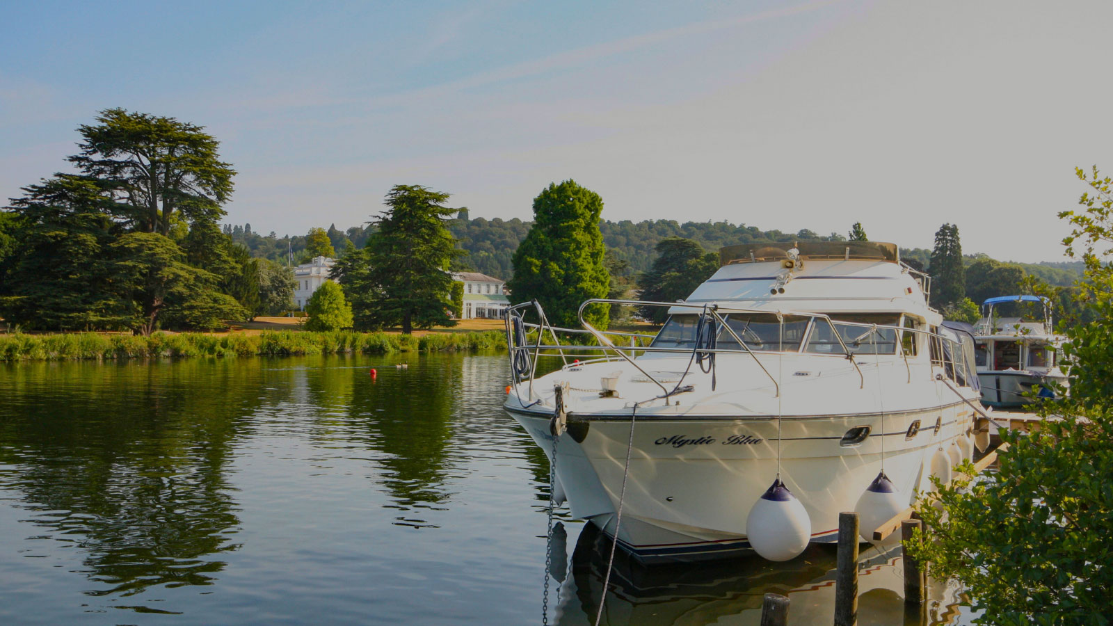 Large white boat moored up along lush green banks of the thames