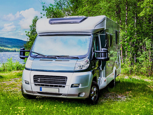 grey motorhome parked beside the thames surrounded by lush green trees