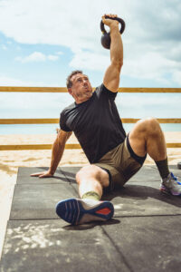 man in workout gear works out on a mat with a weight on a beach