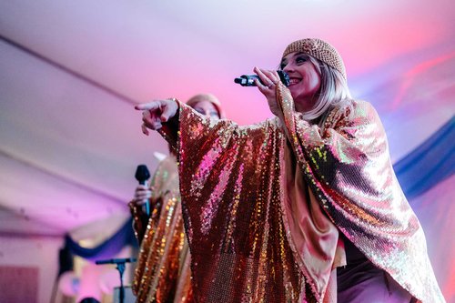 a woman in an abba style costume sings on a stage with a microphone