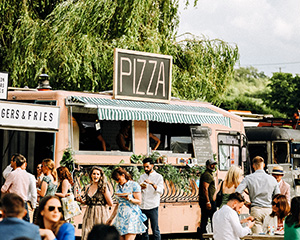 a mobile pizza truck at an outdoor festival with trees behind it