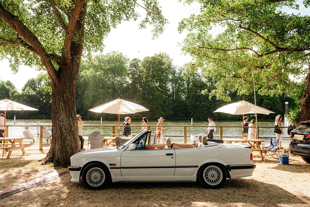 A white car is parked alongside a river on a sunny day