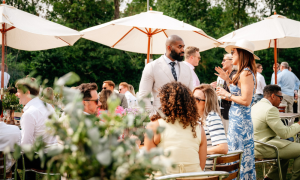 a man and woman, nicely dressed, stand in amongst other people at tables and talk to each other at an outdoor event