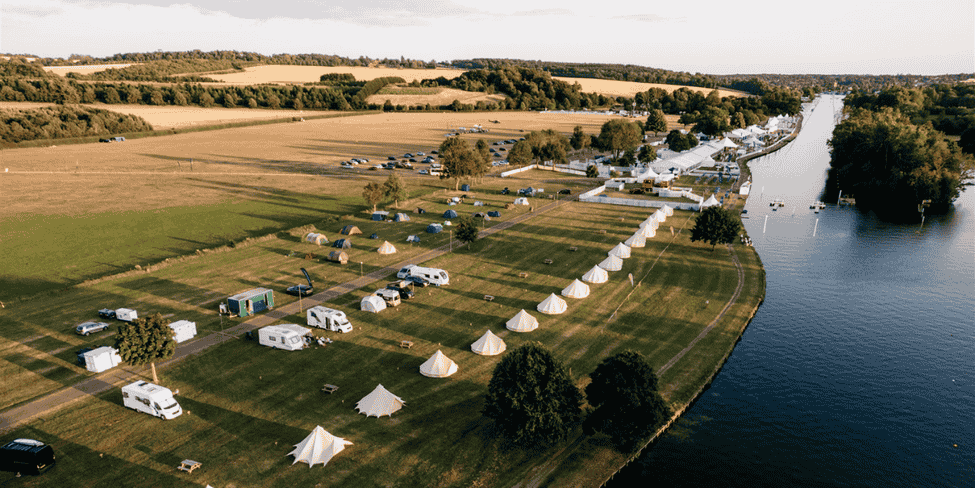 A view over a campsite with bell tents and motorhomes, situated by a river