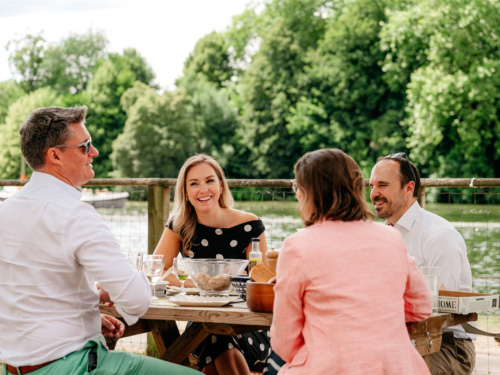 Guests dining at a reserved riverside picnic table overlooking the River Thames during Henley Royal Regatta.