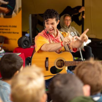 male entertainer wearing a yellow shirt sings to children with his guitar